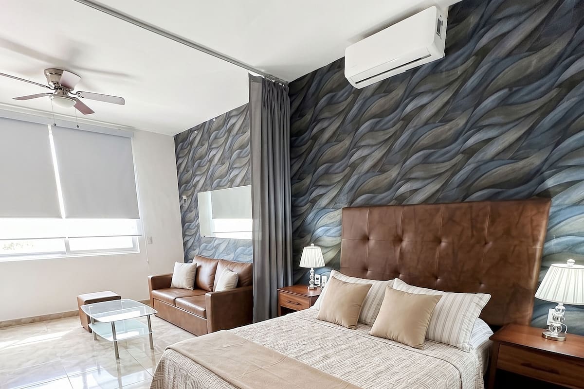 Quarto moderno com uma cama grande, um ventilador de teto, aparelho de ar condicionado, mesa de centro de vidro, mesa de cabeceira e vista para o exterior.