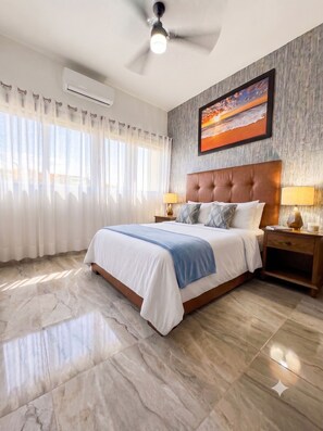 A hotel room with a large bed, a ceiling fan, an air conditioning unit, a nightstand with a lamp, and a painting on the wall. - Las Canoas Zona Romantica By Monyxbnb  (Puerto Vallarta)