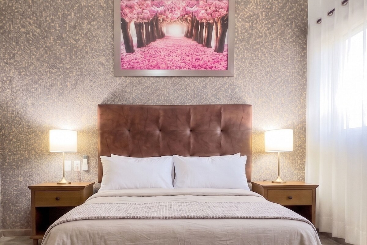Een slaapkamer met een groot bed, twee nachtkastjes met lampen, een marmeren vloer en een muur met een lijstwerkfoto.