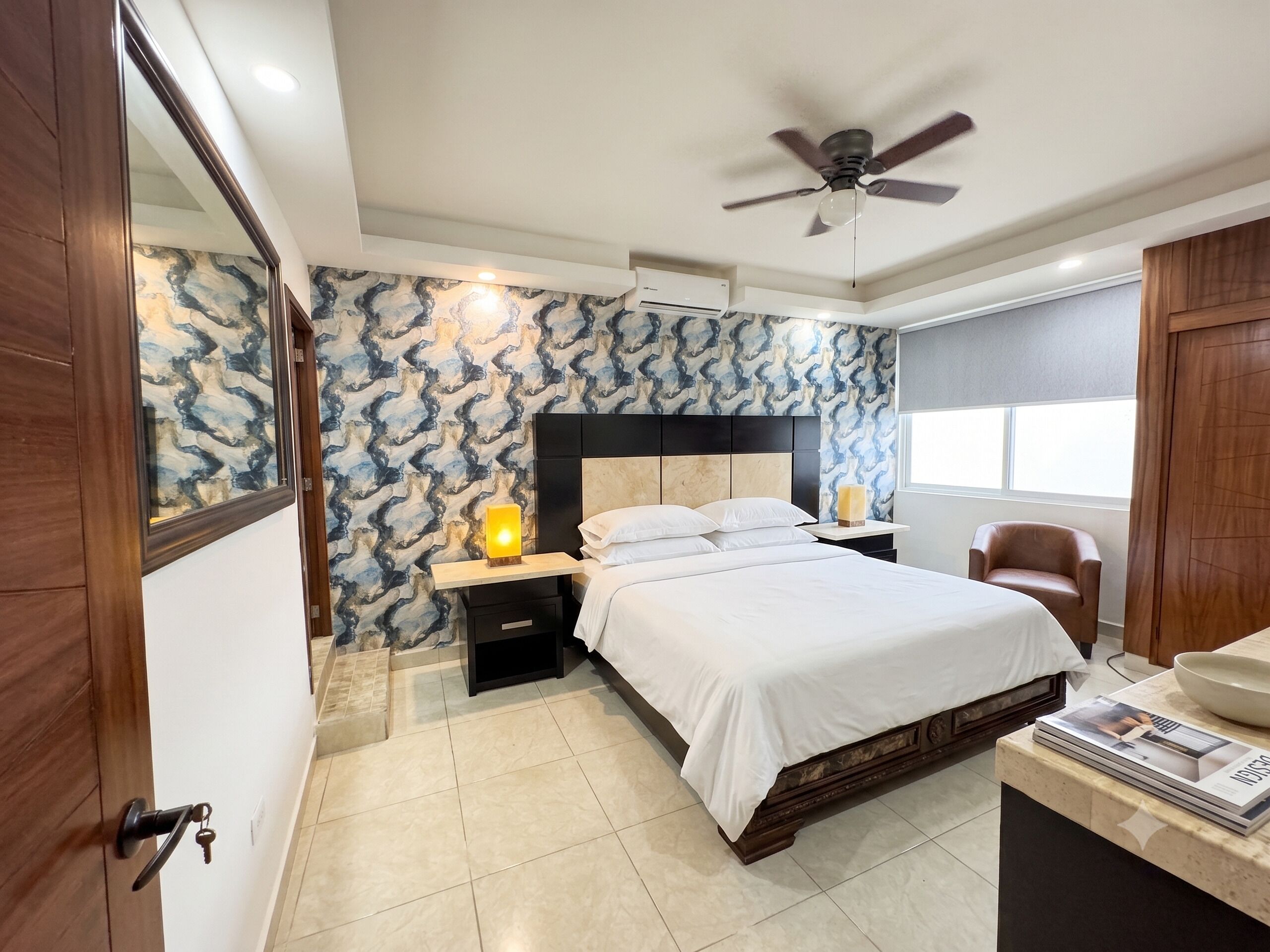 A bedroom with a bed, nightstands, a ceiling fan, a window, and a door.