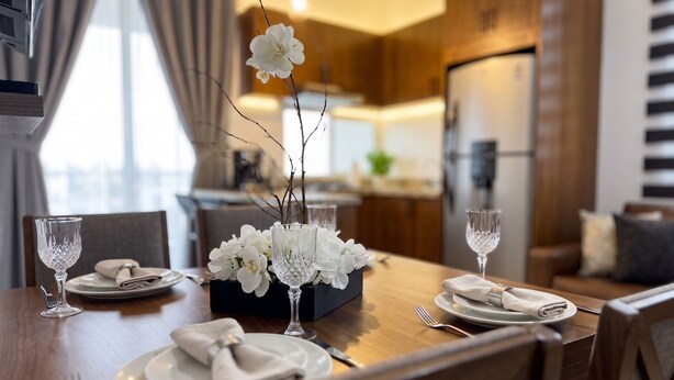 Ein Essbereich mit einem Holztisch, gedeckt für vier Personen, weißen Blumen und einer modernen Küche im Hintergrund.