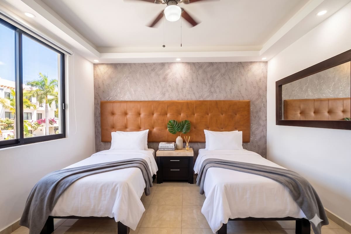 Quarto de hotel com duas camas, uma janela grande, um ventilador de teto e uma parede de mármore.