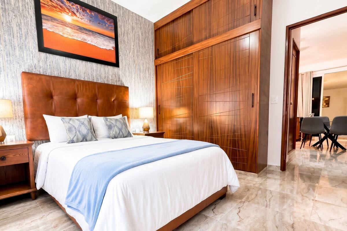 Quarto de hotel com uma cama grande, guarda-roupa de madeira e uma pintura de pôr do sol.