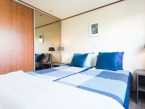 A hotel room with a bed, two bedside tables, a nightstand, a mirror, and a wall-mounted picture. - Holiday Home in Noordwijk With Terrace (Noordwijk)