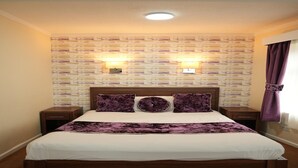A hotel room with a wooden bed, two bedside tables, a headboard, a patterned wallpaper, and a window with curtains. - Deluxe Double Room (Derby)