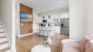 A modern kitchen with white cabinets, a stainless steel refrigerator, and a dining area with stools. - 3008 Whispering Sand C (Panama City Beach)