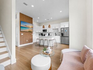 A modern kitchen with white cabinets, a stainless steel refrigerator, and a dining area with stools. - 3008 Whispering Sand C (Panama City Beach)