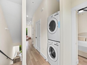 A laundry room with two stacked front-loading washing machines, a staircase, and a hallway leading to a bedroom. - 3008 Whispering Sand C (Panama City Beach)