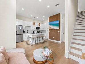 A modern kitchen with white cabinets, a stainless steel refrigerator, a microwave, and a wooden island with bar stools. - 3008 Whispering Sand C (Panama City Beach)