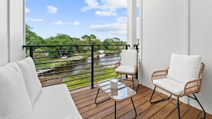 A balcony with wicker chairs, a glass table, and a view of a river and greenery. - 3008 Whispering Sand C (Panama City Beach)