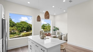 A modern kitchen with a large island, white cabinetry, and a view of a lake and trees. - 3008 Whispering Sand C (Panama City Beach)