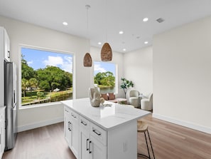 A modern kitchen with a large island, white cabinetry, and a view of a lake and trees. - 3008 Whispering Sand C (Panama City Beach)