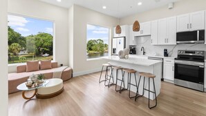 A modern kitchen with white cabinets, a large island, bar stools, and a view of a lake. - 3008 Whispering Sand C (Panama City Beach)