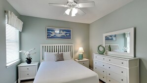 A bedroom with a bed, nightstands, a dresser, a ceiling fan, a window with blinds, and a wall painting. - Poinciana Place #222 - Mystic Miramar (Miramar Beach)
