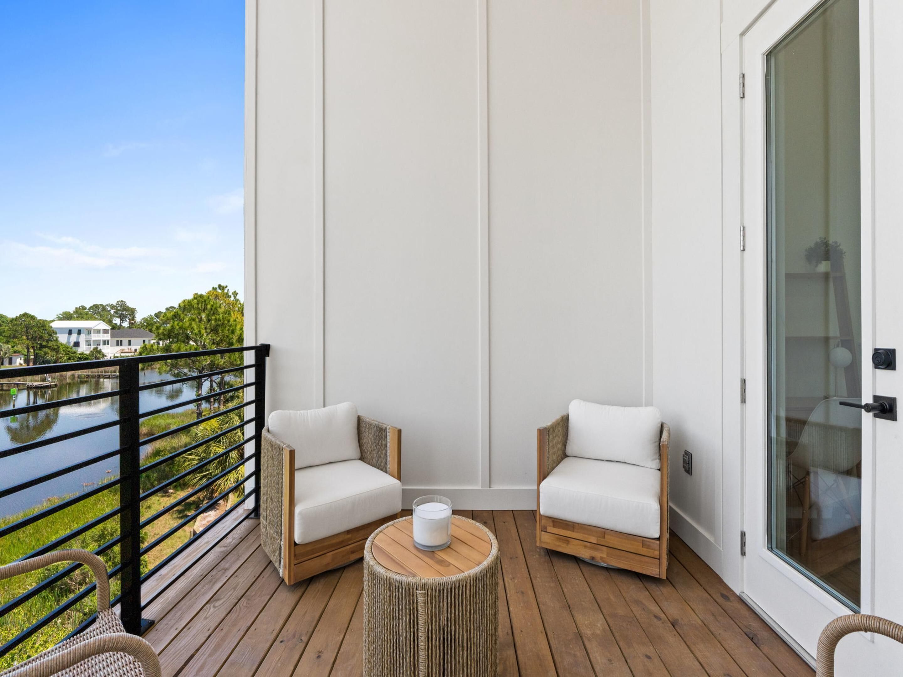 A balcony with two white cushioned chairs, a wicker table, and a view of a body of water.