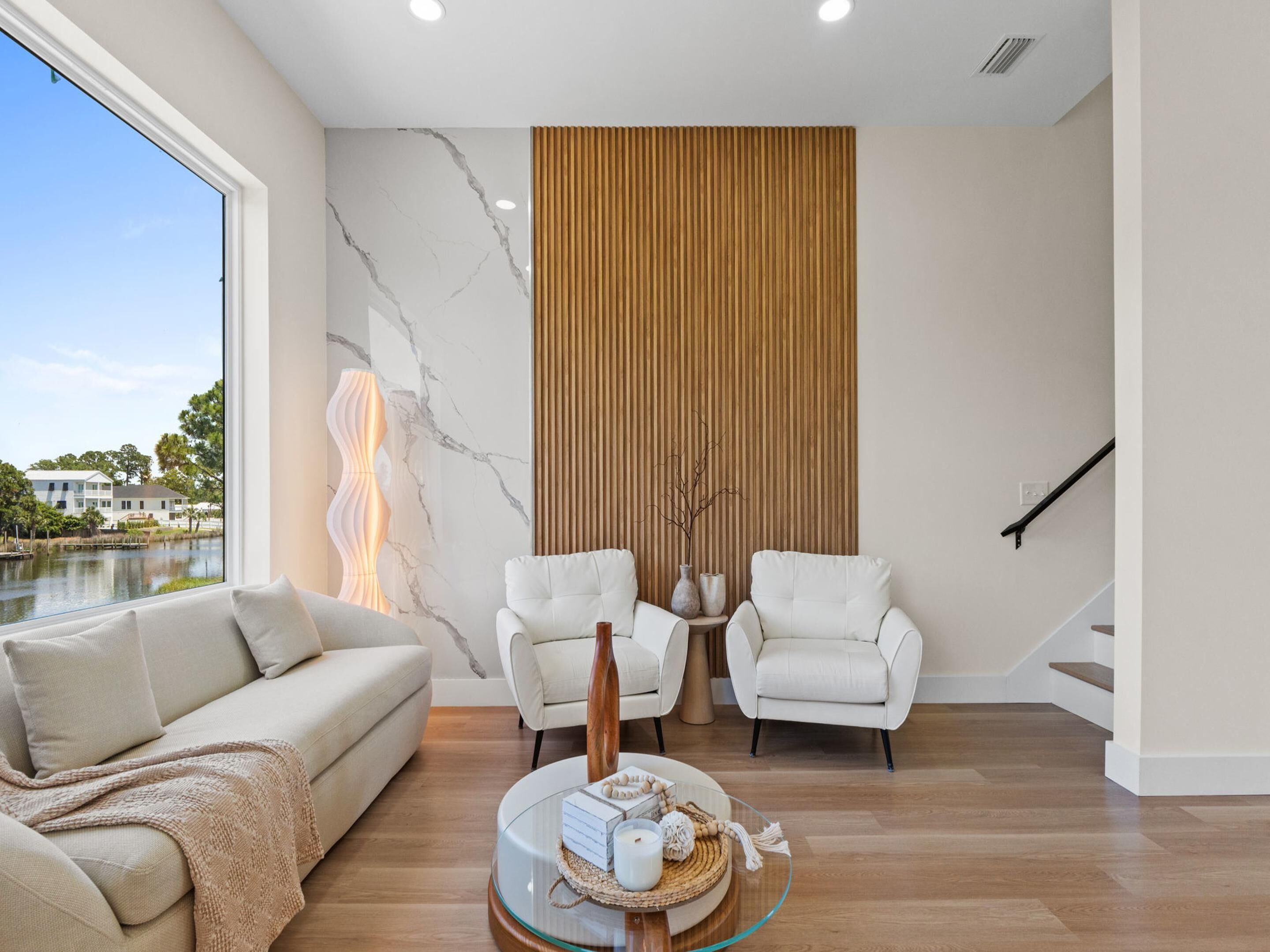 Una sala de estar moderna con un sofá, dos sillones, una mesa de centro de vidrio y vistas a una masa de agua.