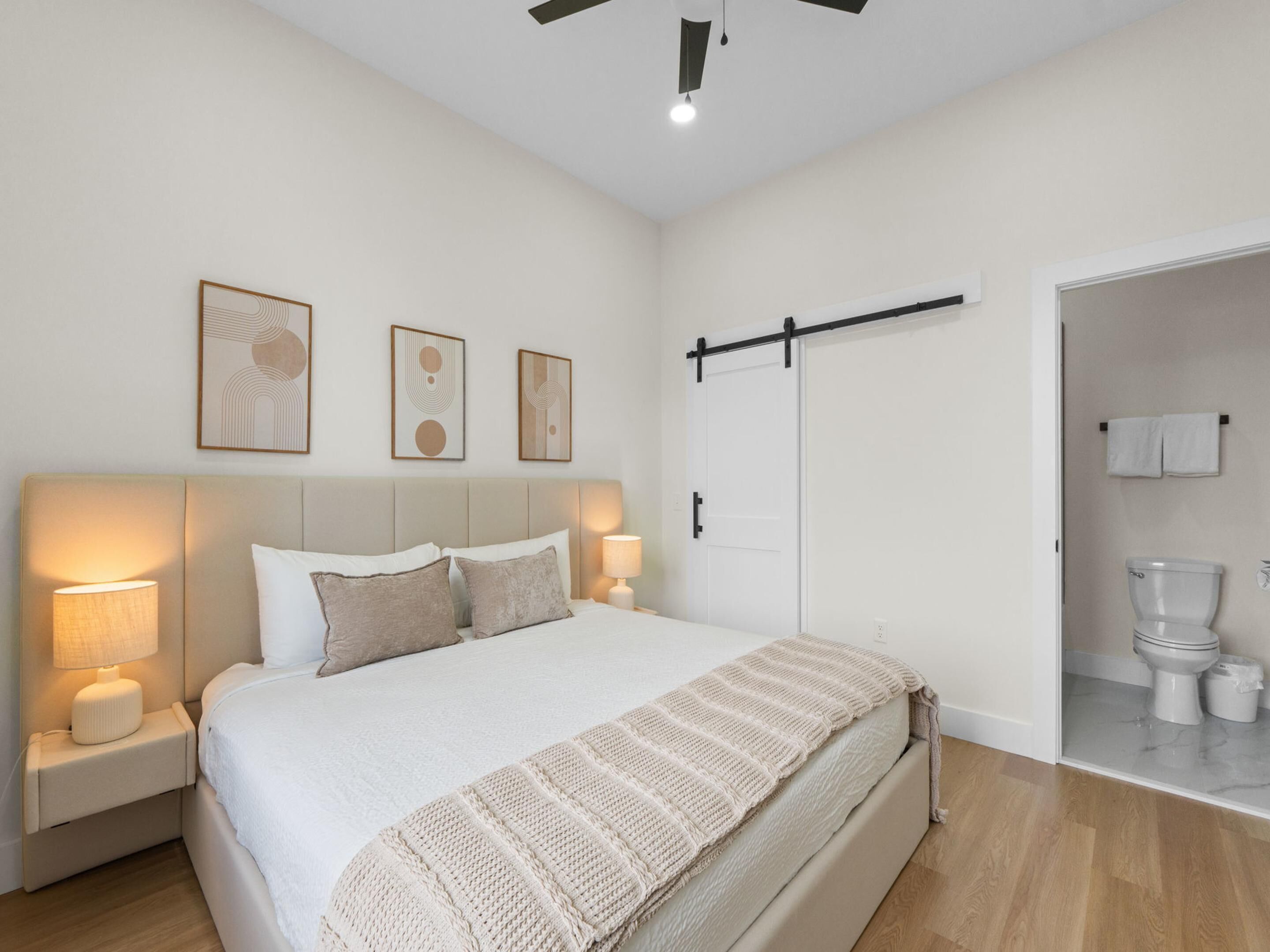 Un dormitorio con cama, mesitas de noche, ventilador de techo y puerta corrediza que da al baño.