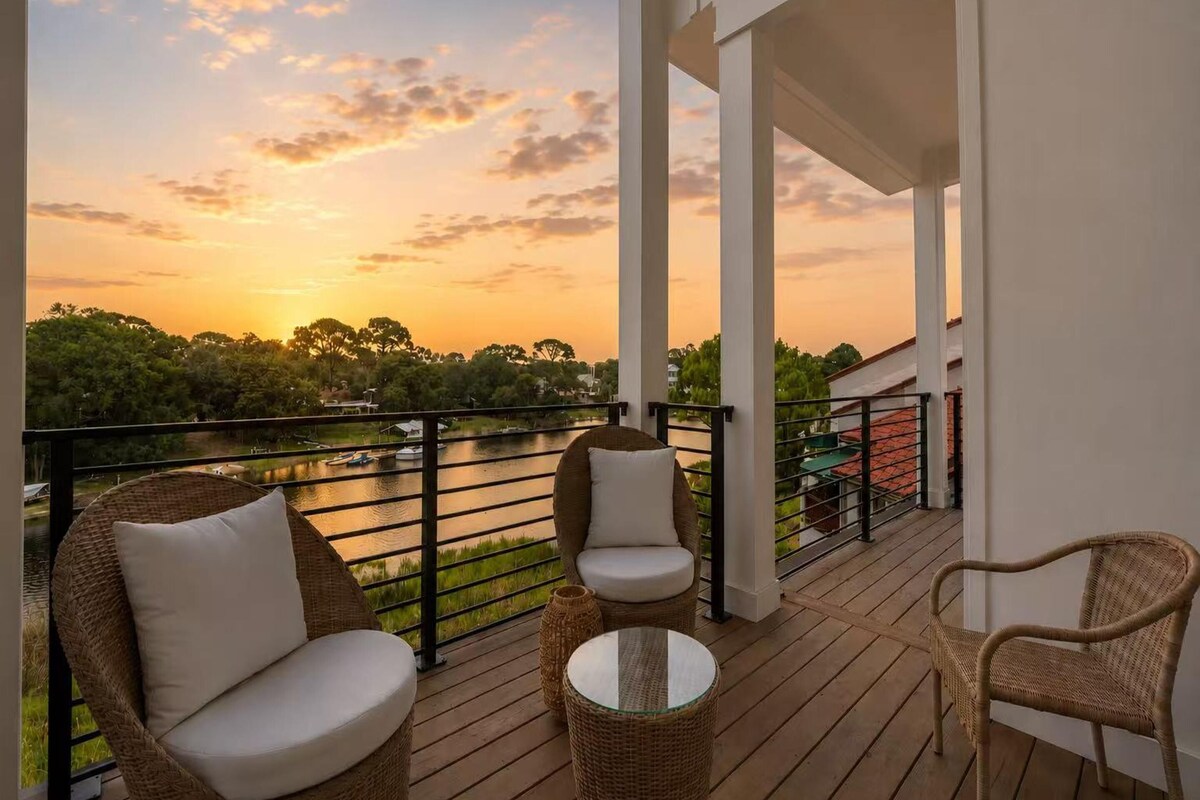 Un balcón con mobiliario de mimbre, vista al río y un atardecer.