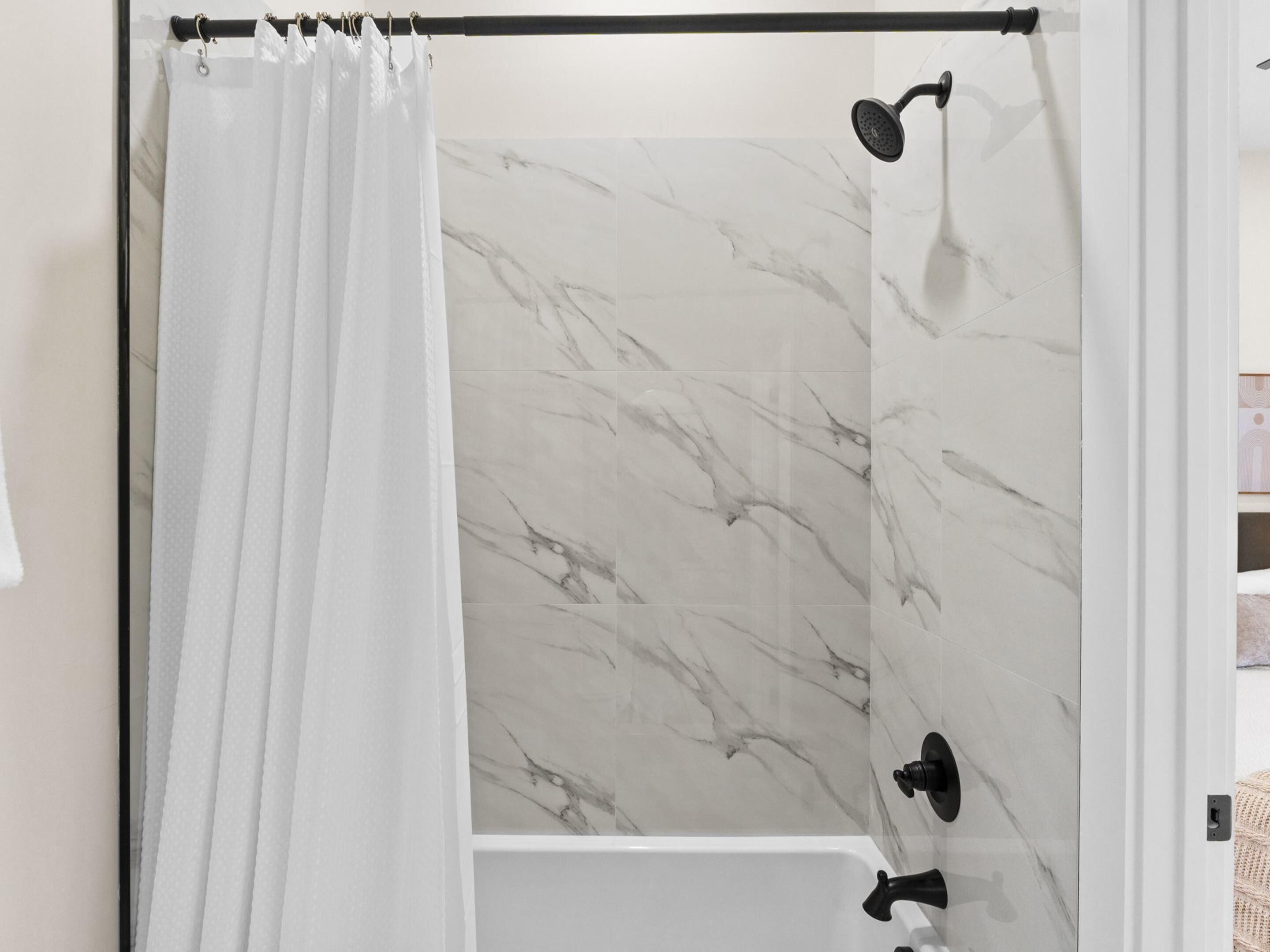 A bathroom with a shower curtain, a handheld showerhead, and a marble-tiled wall.