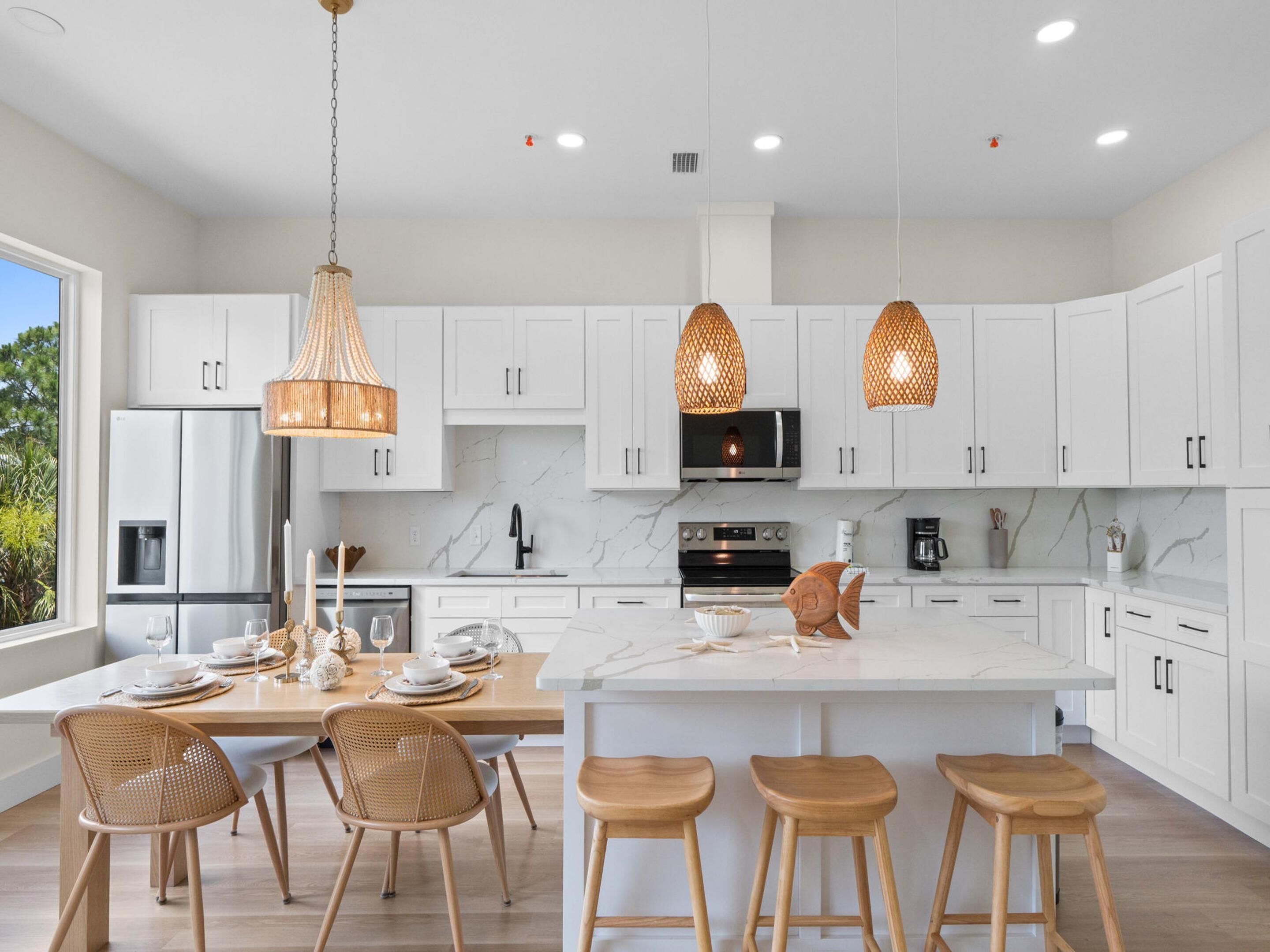 A modern kitchen with white cabinets, a marble countertop, and pendant lights.