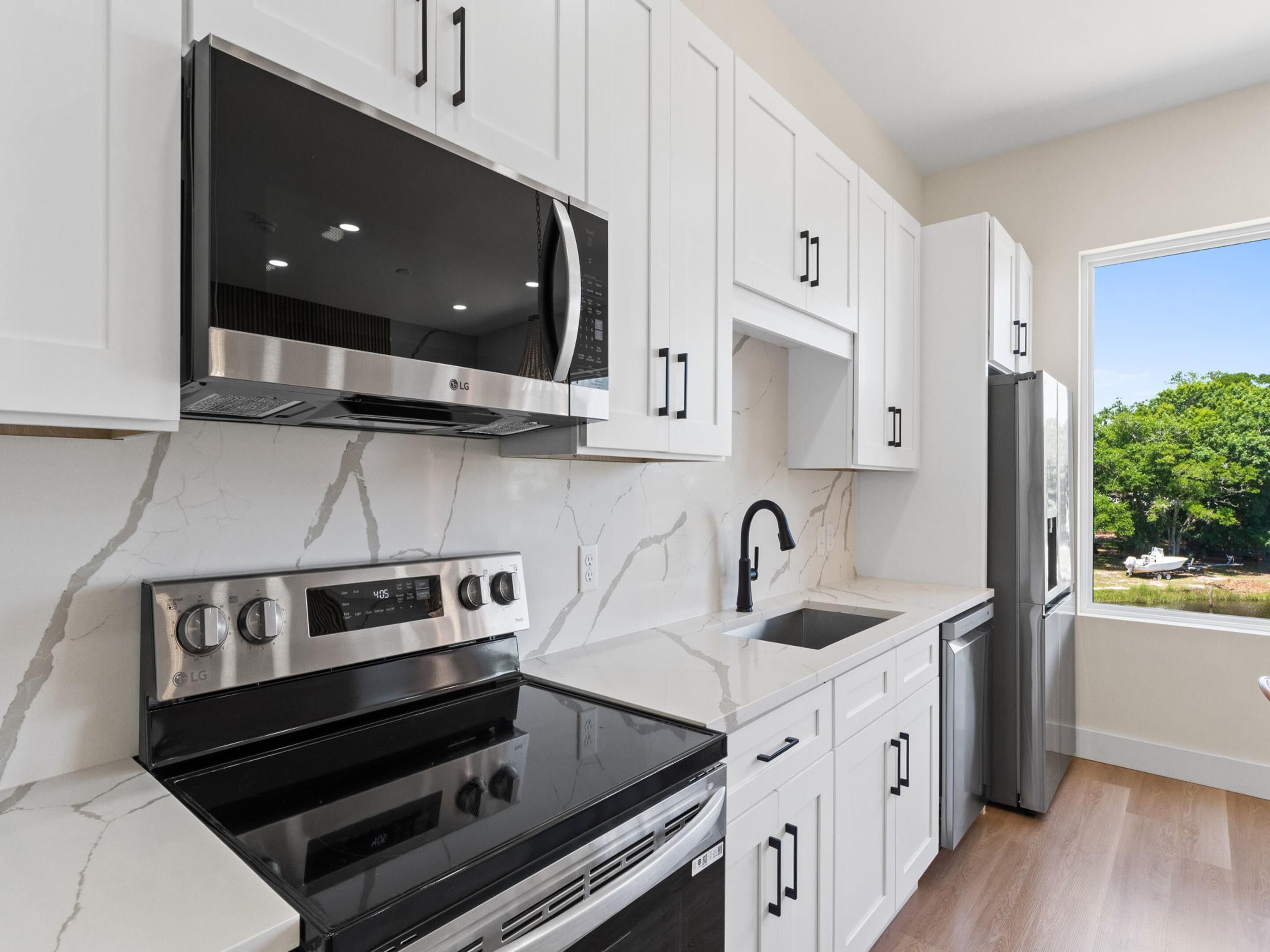 Una cocina moderna con armarios blancos, una estufa de acero inoxidable, un microondas integrado y un refrigerador.