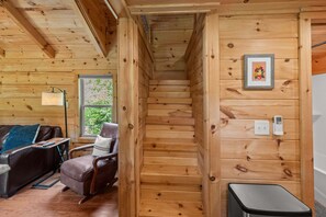 A wooden interior with a staircase, a leather sofa, and a small table. - New River Views - Cozy Cabin with Fire Pit (Todd)