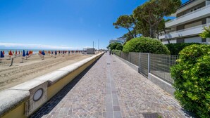 Un vialetto lastricato lungo una spiaggia, con ombrelloni, una recinzione e un edificio con balconi.