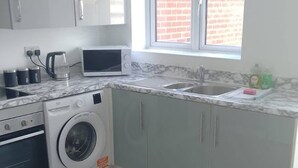 A compact kitchen with a washing machine, a microwave, and a sink. - Huge 4 Bed House with parking and garden! (Bristol)