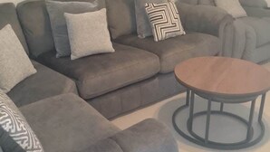 A sectional sofa with multiple pillows, a round coffee table, and a grey armchair in a living room. - Huge 4 Bed House with parking and garden! (Bristol)