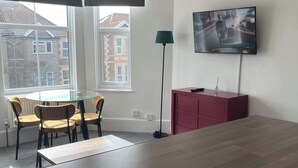 Un soggiorno moderno con un grande tavolo di legno, una TV a muro, una lampada da terra e una finestra con vista sugli edifici.