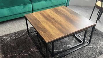 Un canapé vert, une table basse en bois avec des pieds en métal et un tapis à motifs.