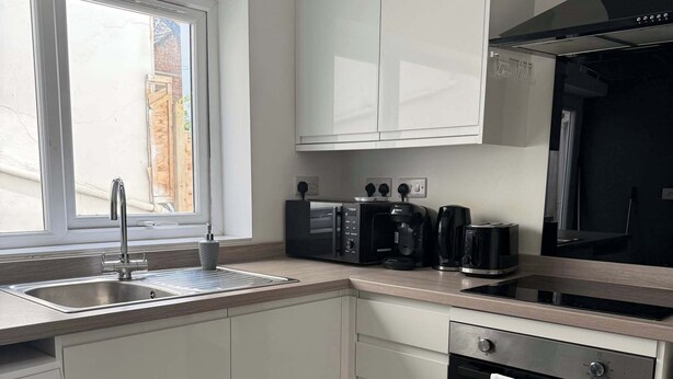 A modern kitchen with white cabinets, a built-in oven, a microwave, a coffee maker, and a sink. - Ground Floor Flat with Courtyard garden (Weston-super-Mare)