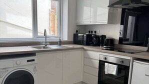 A modern kitchen with a washing machine, oven, microwave, and a window with a view of the outside. - Ground Floor Flat with Courtyard garden (Weston-super-Mare)