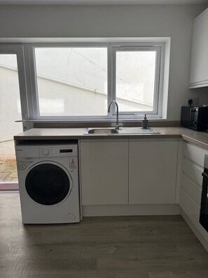 Eine kompakte Küche mit Einbauwaschmaschine, Spüle und Fenster über der Arbeitsfläche.