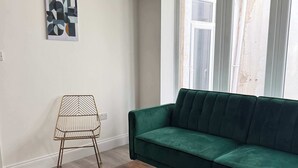 A living room with a green sofa, a wooden coffee table, a patterned chair, and a painting on the wall. - Ground Floor Flat with Courtyard garden (Weston-super-Mare)