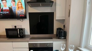 A modern kitchen with white cabinetry, a microwave, a stove, and a dining table set with blue plates and glasses. - 1 Bed Room Flat Close to seafront (Weston-super-Mare)