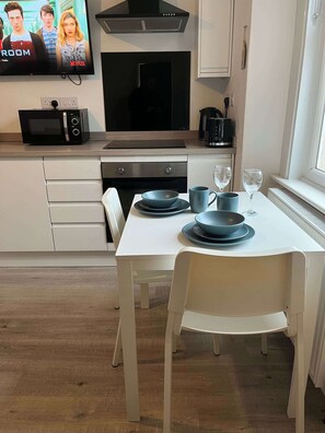 Ett modernt kök med vita köksskåp, en mikrovågsugn, en spis och ett matbord med blå tallrikar och glas.