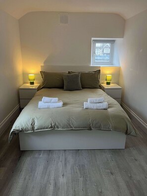 A neatly made bed with two pillows, two bedside lamps, and two folded towels on the headboard. - 1 Bed Room Flat Close to seafront (Weston-super-Mare)