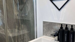 A bathroom with a glass-enclosed shower, a white sink, and three black bottles labeled shampoo, shower gel, and conditioner. - 1 Bed Room Flat Close to seafront (Weston-super-Mare)