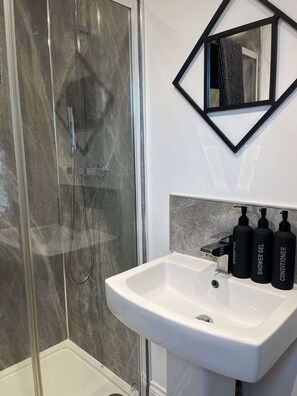 A bathroom with a glass-enclosed shower, a white sink, and three black bottles labeled shampoo, shower gel, and conditioner. - 1 Bed Room Flat Close to seafront (Weston-super-Mare)