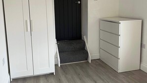 A room with a wardrobe, a dark door, a small step leading to a lower level, and a white dresser. - 1 Bed Room Flat Close to seafront (Weston-super-Mare)