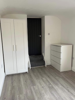 A room with a wardrobe, a dark door, a small step leading to a lower level, and a white dresser. - 1 Bed Room Flat Close to seafront (Weston-super-Mare)