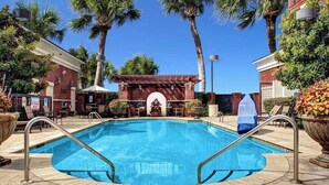 A swimming pool with a 3 FT depth marker, surrounded by palm trees and a brick building.