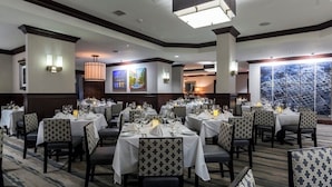 A restaurant with multiple tables set for dining, featuring patterned chairs and a carpeted floor.