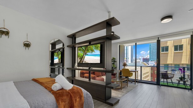 Ein modernes Hotelzimmer mit Bett, Fernseher, einem Balkon mit Blick auf die Stadt und einer Sitzecke mit Tisch und Stühlen.