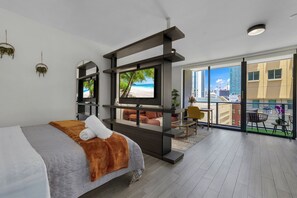 A modern hotel room with a bed, a TV, a balcony with a view of the city, and a seating area with a table and chairs. - Miami Bayside Balcony Studio Pool & Gym (Miami)