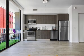 A modern kitchen with stainless steel appliances, a dining area with a glass partition, and a view of a red building outside. - Miami Bayside Balcony Studio Pool & Gym (Miami)