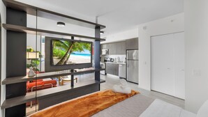 Ein modernes Hotelzimmer mit Bett, Fernseher, Küchenzeile und Blick auf einen Strand.