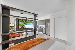 A modern hotel room with a bed, a TV, a kitchen area, and a view of a beach. - Miami Bayside Balcony Studio Pool & Gym (Miami)