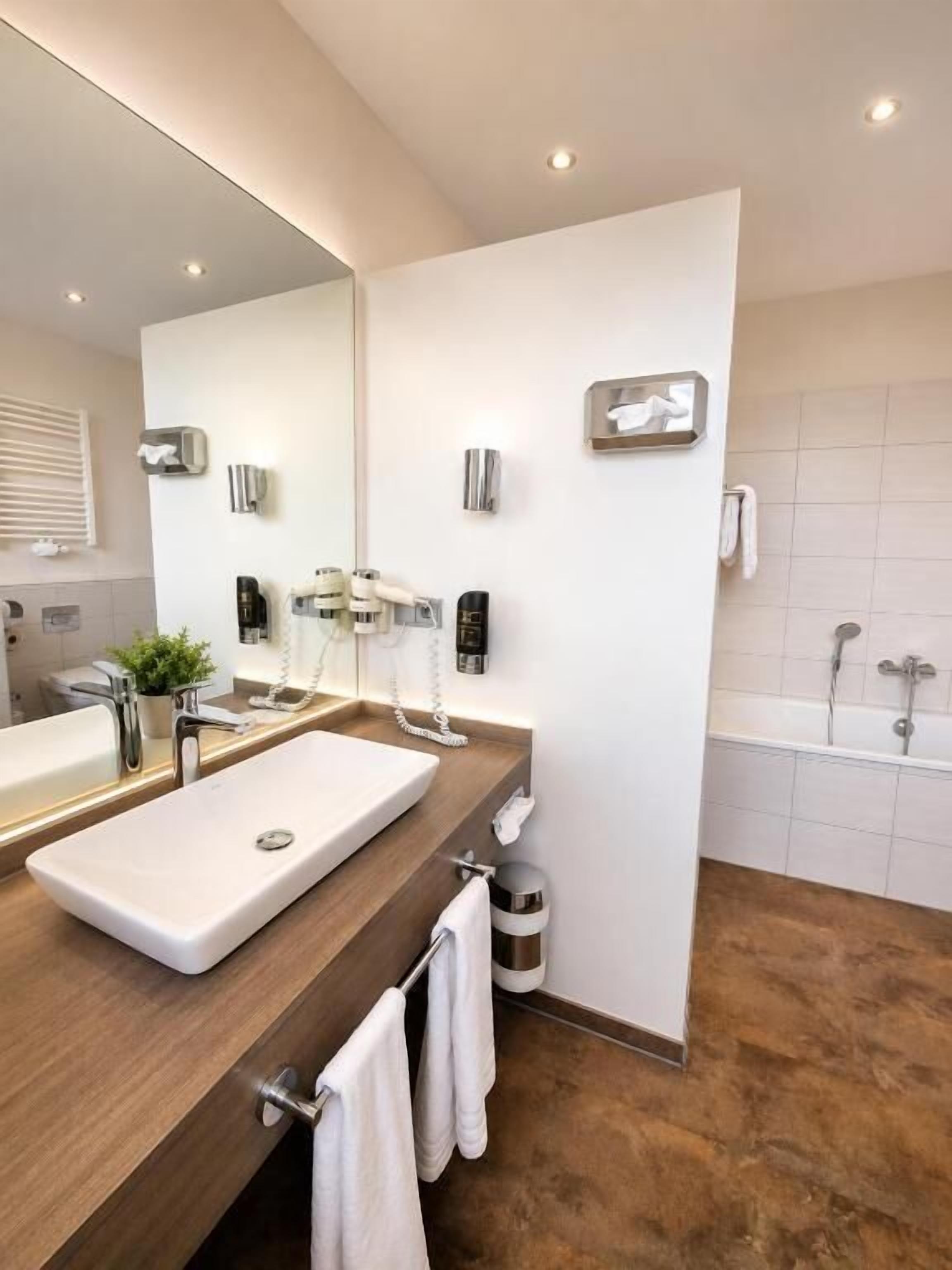 Un baño moderno con un espejo grande, dos lavamanos, una bañera y un perchero para toallas.